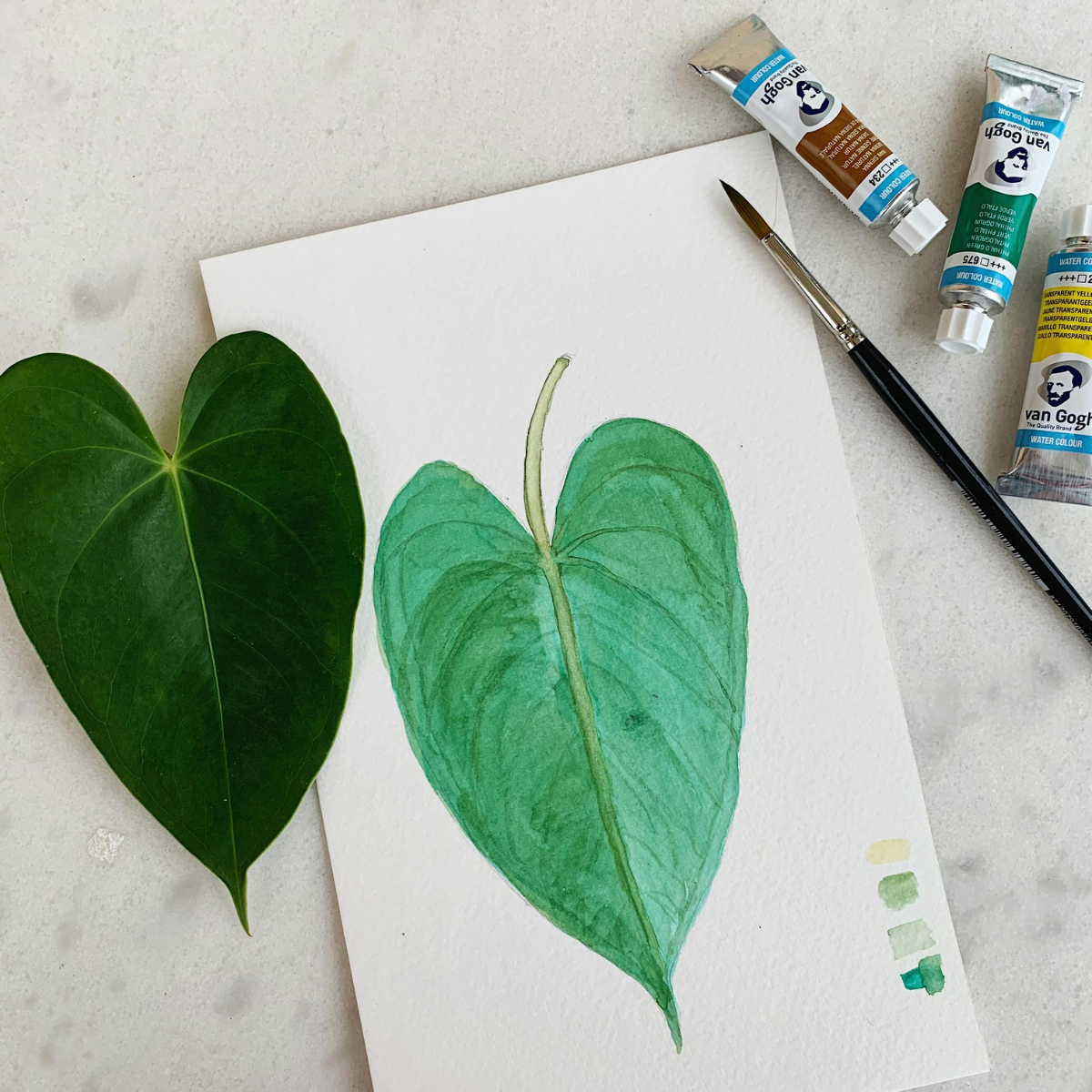 Painting of a green leaf on paper with Van Gogh paint tubes and brush.